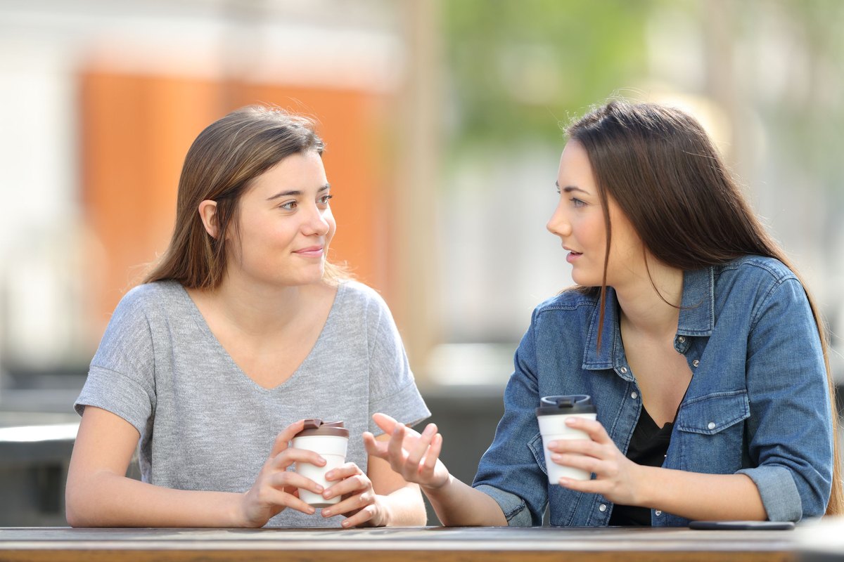 Two casual friends talking in a park drinking coffee