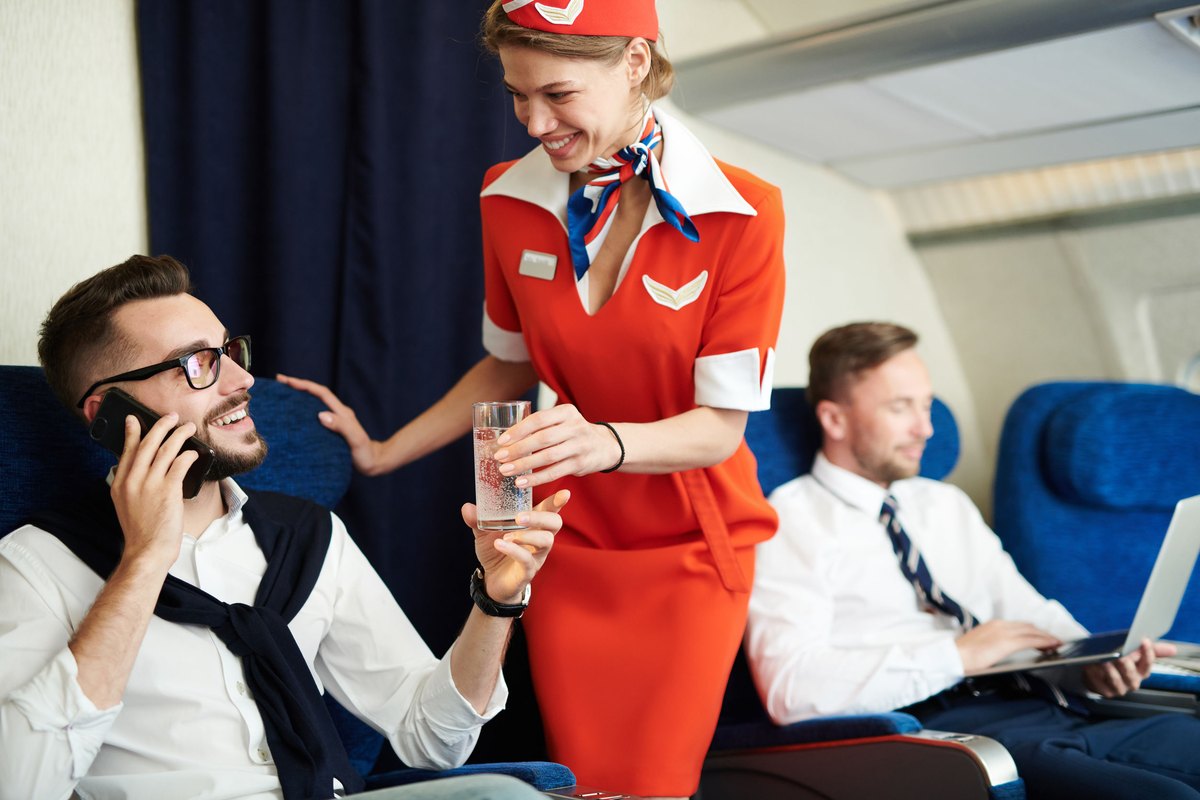 Portrait of smiling flight attendant serving glass sparkling water to handsome businessman enjoying first class trip, copy space